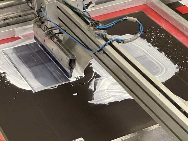 Diese Rakel trägt deckendes Weiß auf eine schwarze Platte auf